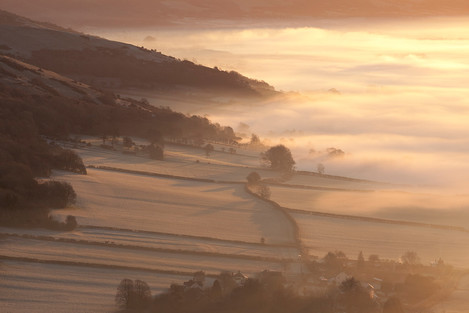 Early morning mist swirls around the base of Compton Hill and Wavering Down in Somerset.  Just visible through the mist is Compton Bishop village surrounded by fields enclosed with traditional hedgerows.  Part of the Mendip Hills AONB.