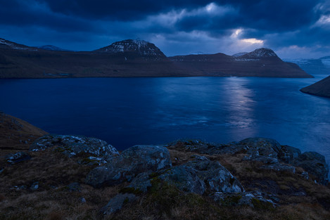 A dark sunset, photographed below Klakkur (413 m). Below the sun the village of Leirvík, barely visible.